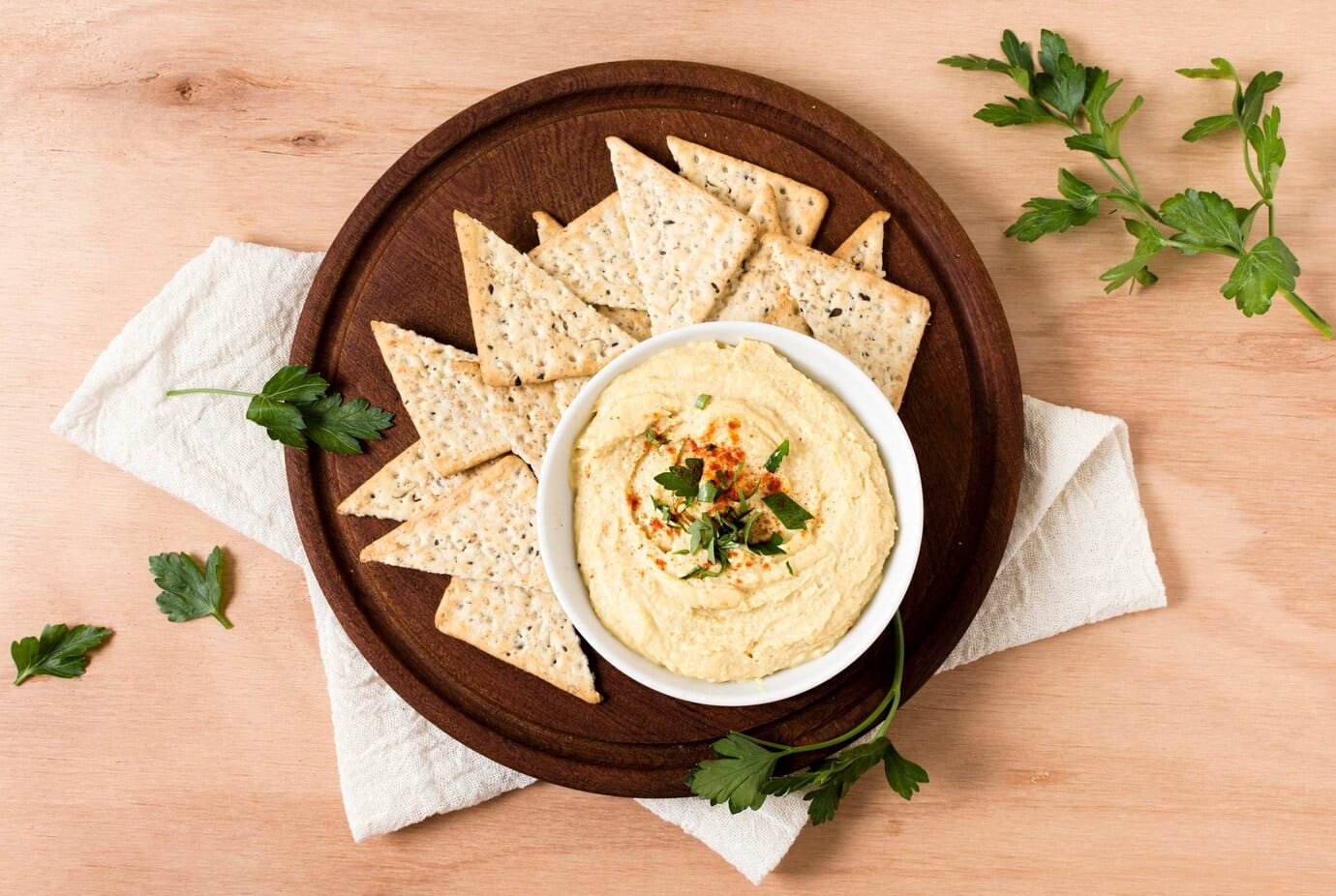 wooden platter holds a bowl of creamy dips topped with herbs and paprika
