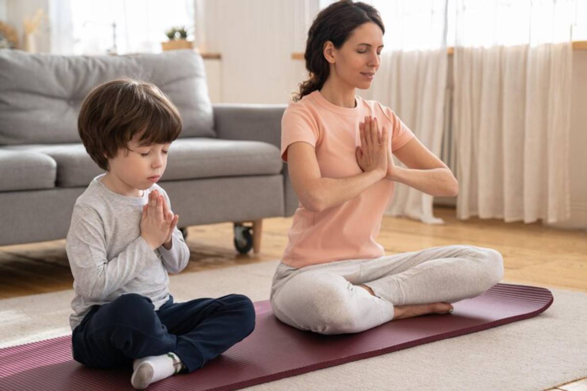 A woman and a child practice yoga together on a mat in a serene living room, both with hands in a prayer position.
