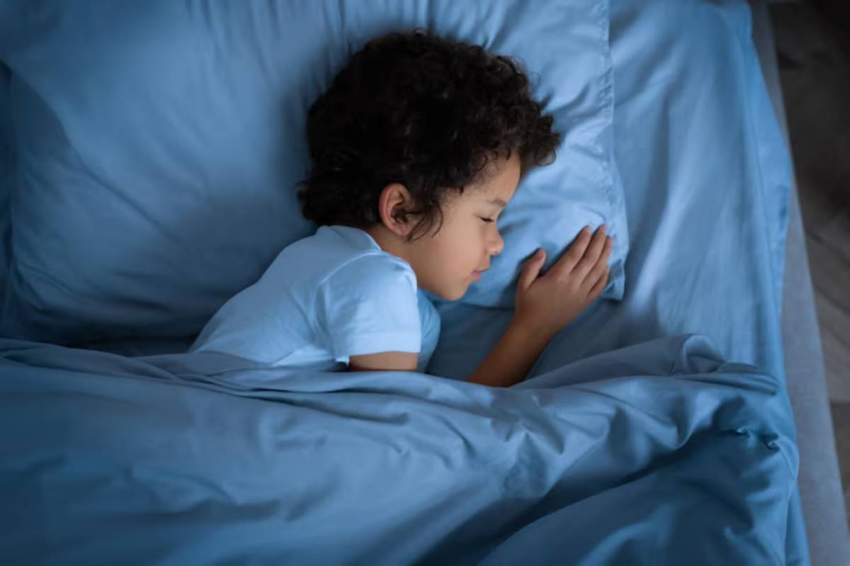 A child softly sleeps on a bed with light blue sheets, curled up with hands tucked alongside, embracing a peaceful moment.