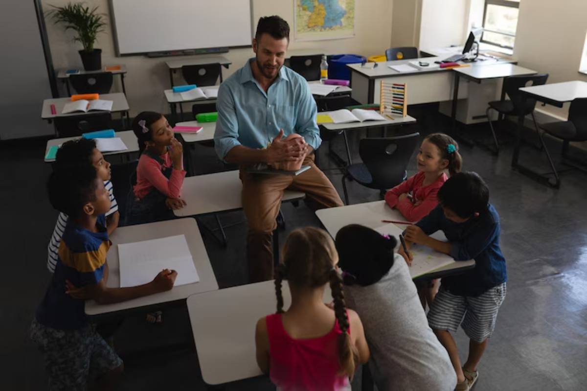 A teacher engages with a group of diverse children seated at desks in a bright classroom, fostering interaction and learning.