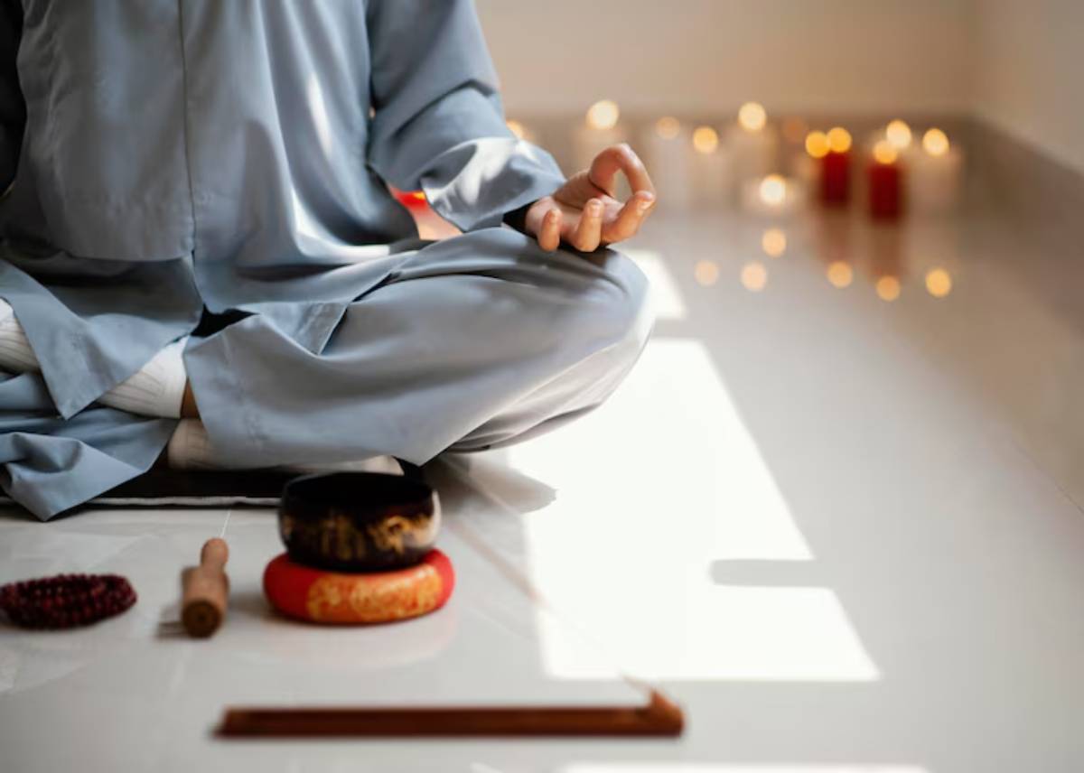 A person in a blue robe meditates on a floor with candles and meditation tools, embodying peace and tranquility.