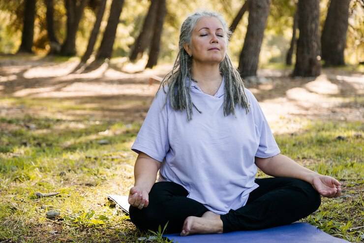 A person sits cross-legged on a yoga mat in a serene forest, practicing meditation amidst dappled sunlight and tall trees.
