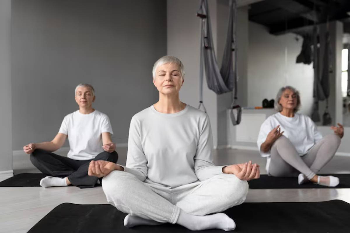 Three people meditate in a bright, modern studio, surrounded by yoga mats and aerial silk equipment, promoting a calm atmosphere.