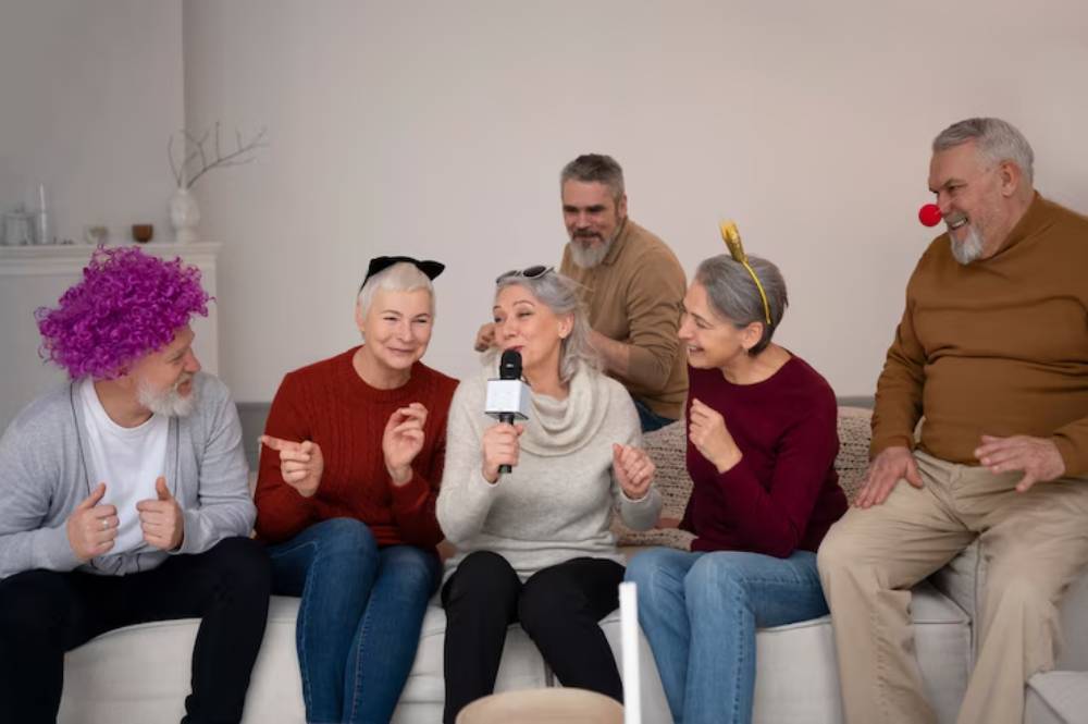 A group of cheerful seniors, some wearing playful costumes, engage in a lively conversation on a couch in a cozy setting.