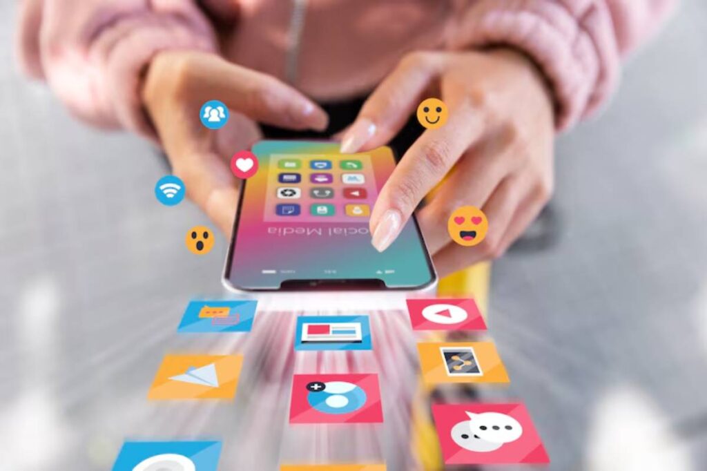 A person holds a smartphone displaying colorful app icons, with various reaction emojis floating above, symbolizing social media engagement.