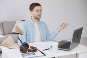A person sits at a desk with a laptop, headphones, and a cup, practicing mindfulness in a bright, modern workspace.